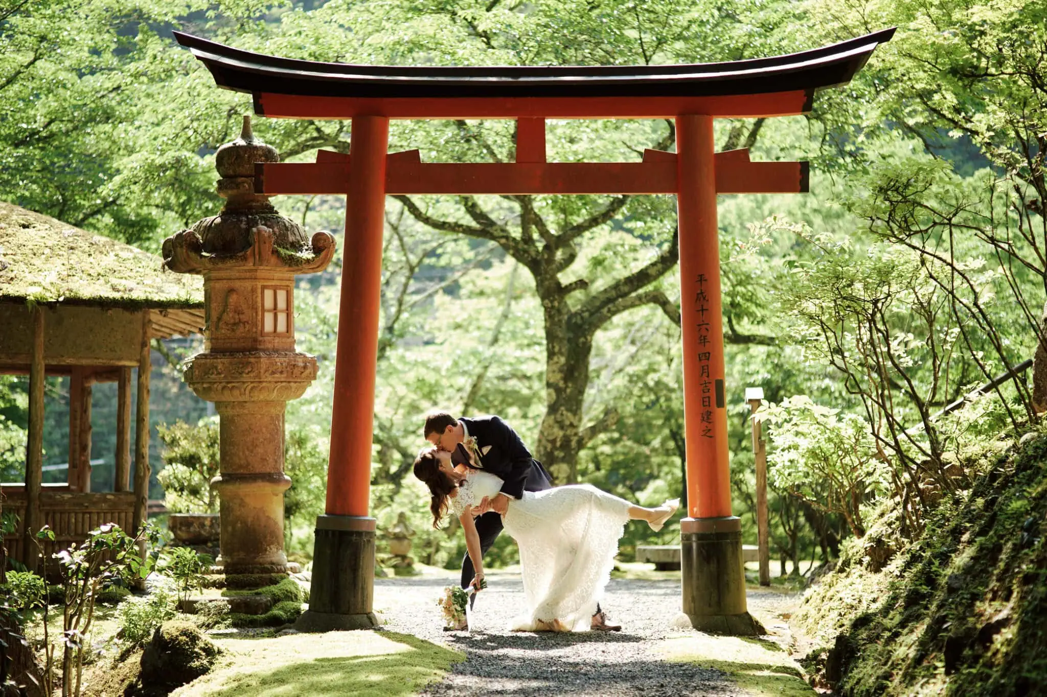 queenstown new zealand heli wedding elopement photographer videographer | A couple in wedding attire poses under a red torii gate in a lush garden with green trees and a stone lantern, captured beautifully by a Queenstown Wedding Photographer.