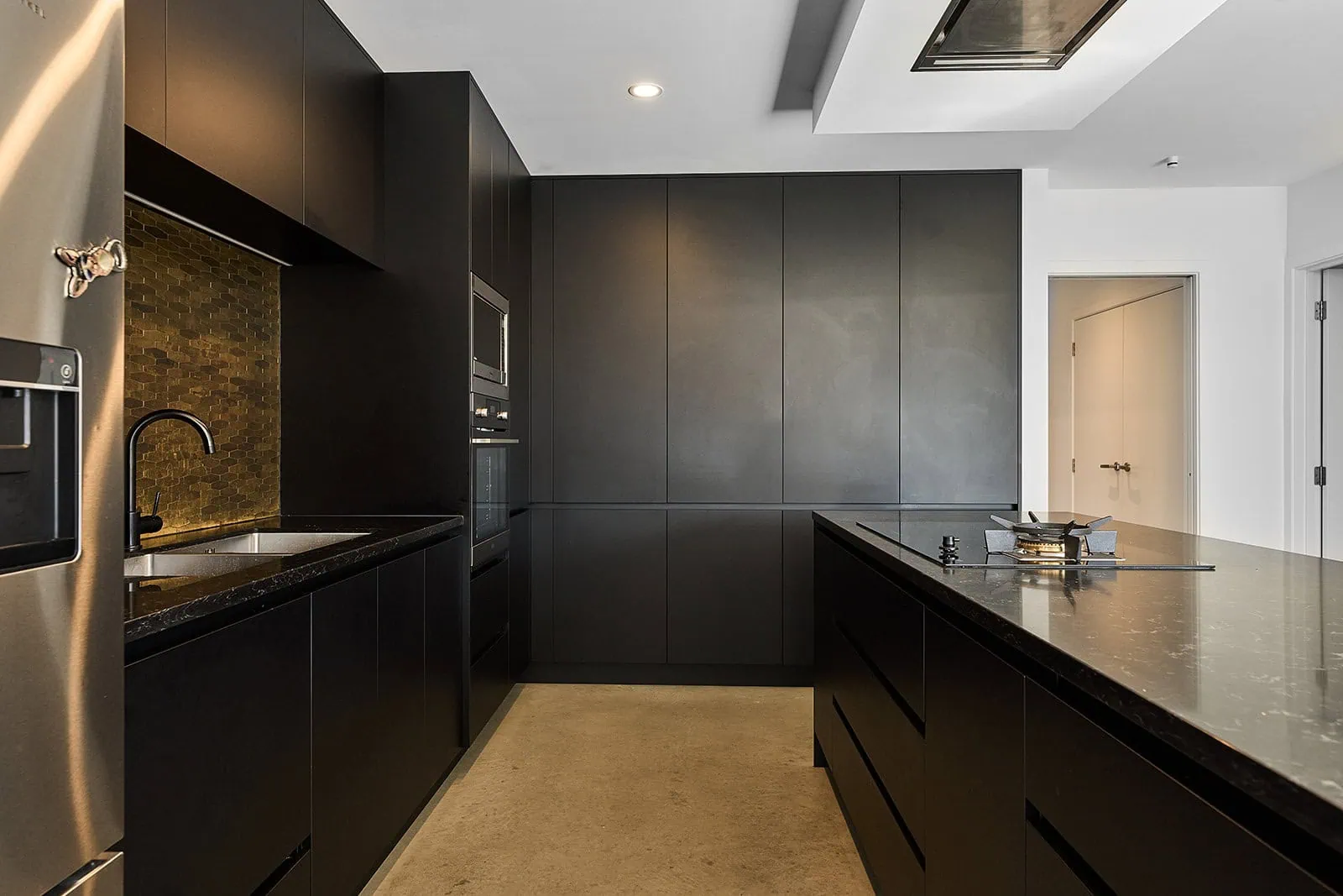 queenstown new zealand heli wedding elopement photographer videographer | Modern kitchen in Jacks Point with matte black cabinets, built-in appliances, an island with a black countertop, and a mosaic tile backsplash under bright ceiling lighting—perfect for your Queenstown AirBnB experience.