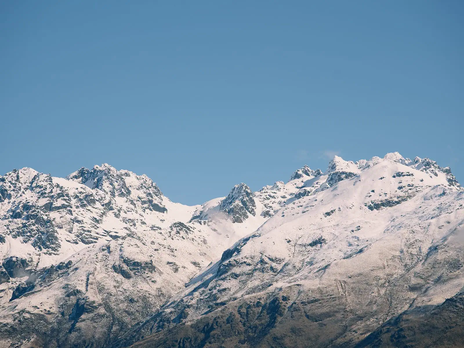 queenstown new zealand heli wedding elopement photographer videographer | Snow-covered mountain peaks rise under a clear blue sky, capturing the beauty of Jacks Point near Queenstown—an ideal AirBnB retreat for nature lovers.